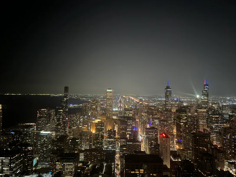 Chicago, Illinois skyline at night from the 360 Chicago observation deck on the 94th floor, with city lights illuminating skyscrapers across the Magnificent Mile
