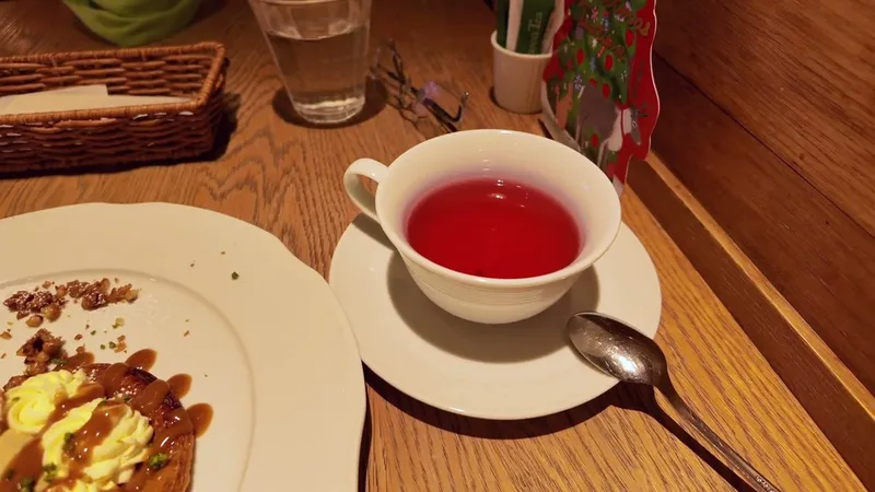 Close-up of a cup of red fruit tea next to a cream and nut dessert on a wooden table at Afternoon Tea in Tokyo Skytree Town, Japan