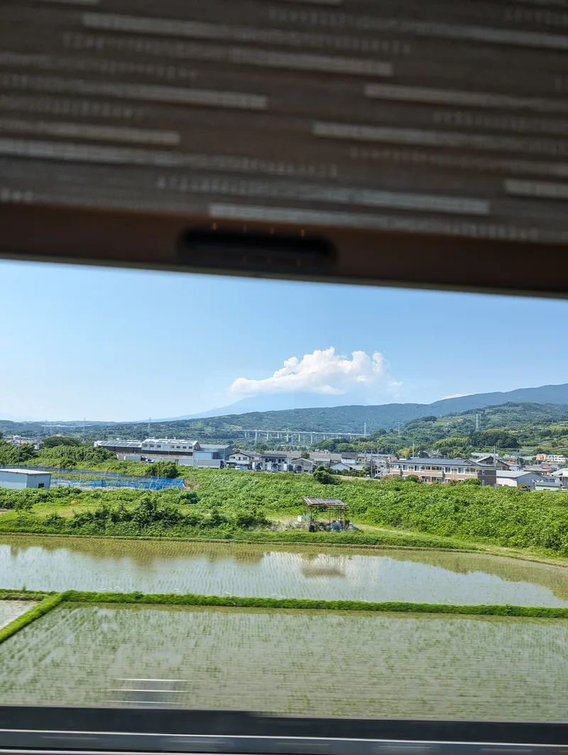 Scenic view from a Shinkansen window of lush green rice paddies, houses, and distant mountains in Japan.