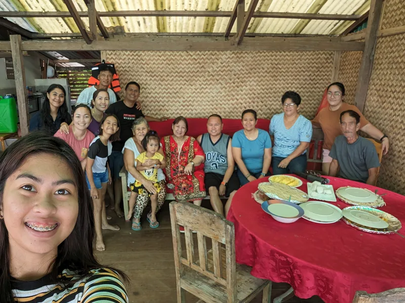 Large group of family and friends gathered together for a group selfie in a rustic outdoor dining area in Palawan, Philippines