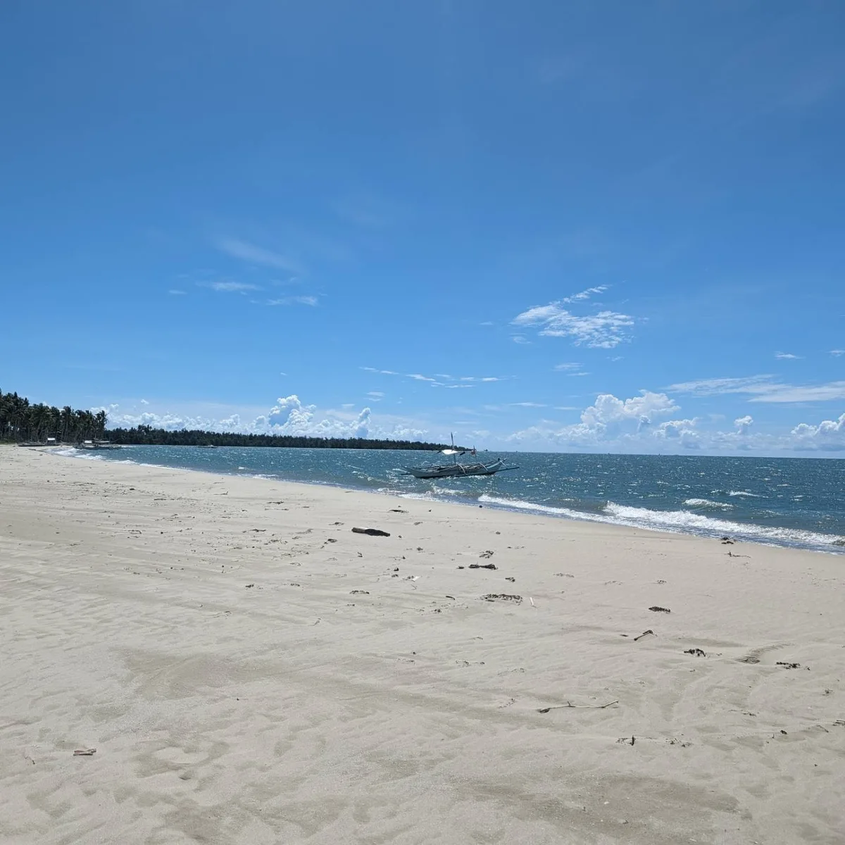 Wide shot of a pristine sandy beach in Palawan, Philippines with gentle waves and traditional outrigger bangka boats on the shore