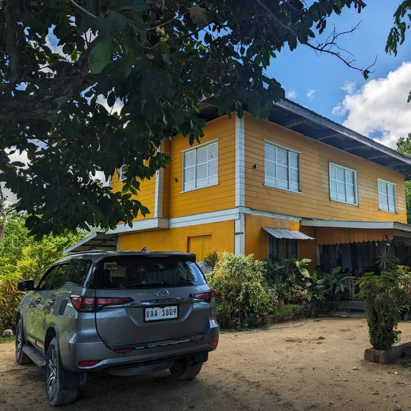 Grey Toyota Fortuner SUV parked on a dirt path in front of a yellow two-story house in Busuanga, Caramay, Palawan
