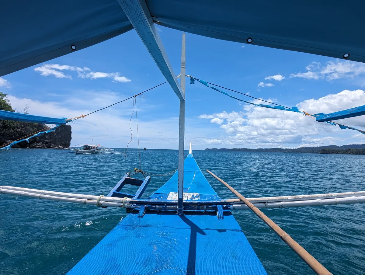 View from the front of a Filipino bangka boat heading across clear blue ocean toward the islands near Sabang, Palawan, Philippines