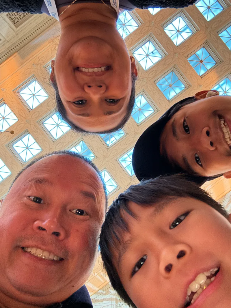 Family of four taking a low-angle selfie at the Field Museum in Chicago, Illinois with ornate ceiling above