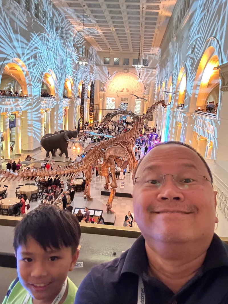 Father and son selfie in the grand hall of the Field Museum in Chicago, Illinois with dinosaur skeletons and event lighting