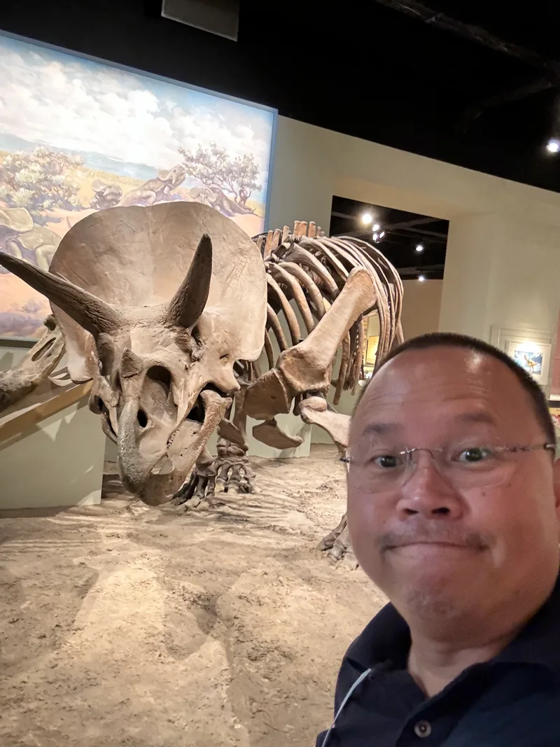 Man taking a selfie with a Triceratops skeleton at the Field Museum in Chicago, Illinois