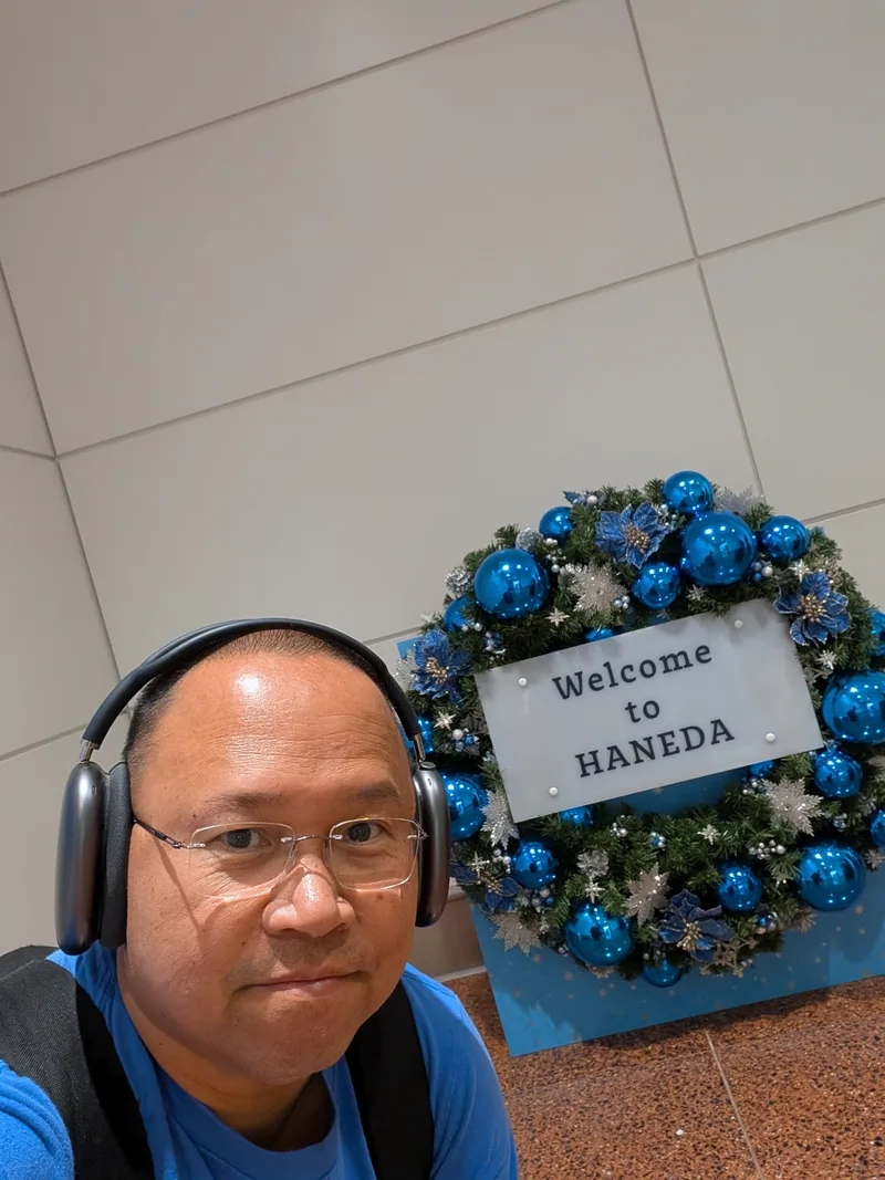 Man taking selfie next to a blue and silver Welcome to Haneda Christmas wreath at Haneda Airport, Tokyo, Japan