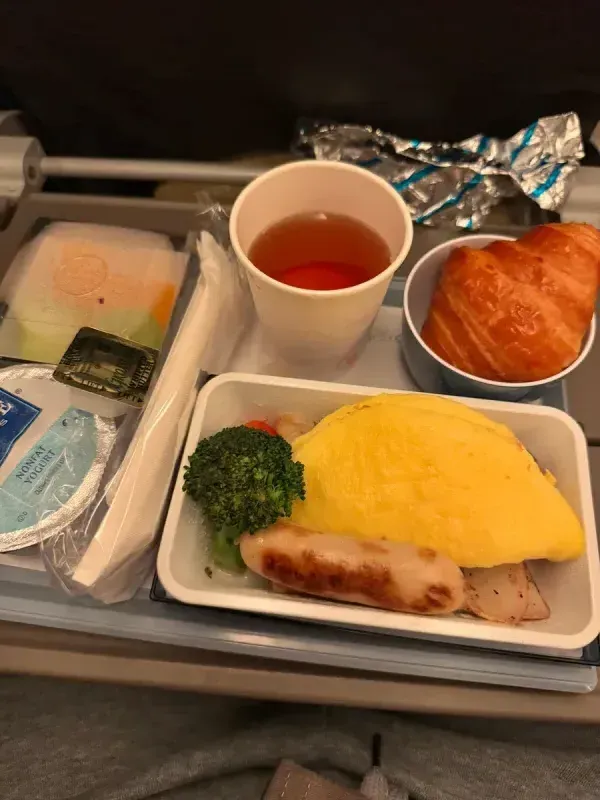 Airplane breakfast with omelet, sausage, croissant, yogurt, and tea