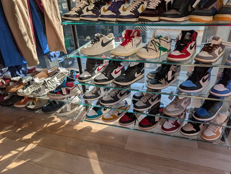 Interior of a Harajuku secondhand store with sneakers lined up on glass shelves and sunlight on the wooden floor in Tokyo, Japan