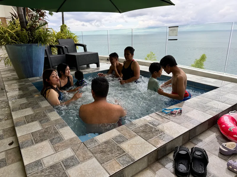 The jacuzzi at Casa Amara — it runs cold, not heated, but the view compensates — Batangas, Philippines Family and friends relaxing in an outdoor jacuzzi with a panoramic ocean view and green umbrella overhead at Casa Amara, Batangas, Philippines.