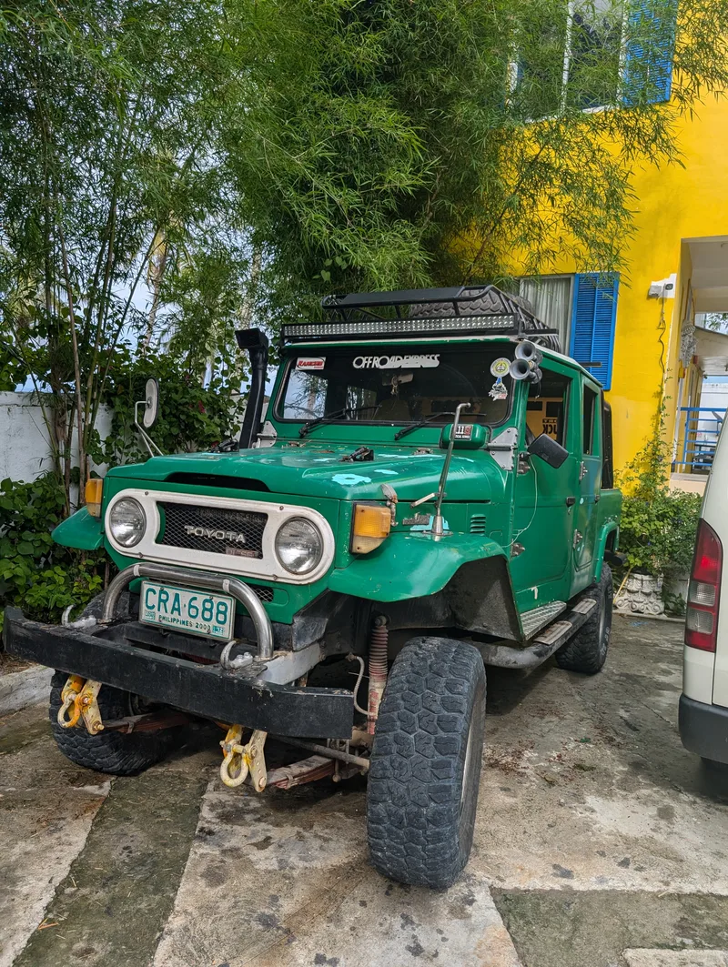 The Land Cruiser at Casa Amara — later identified as a 1978–1982 70 Series, running 33-inch tires Bright green vintage Toyota Land Cruiser with roof rack, snorkel, and large off-road tires parked in front of a yellow building with bamboo at Casa Amara, Batangas, Philippines.