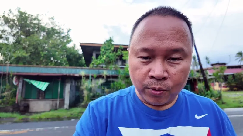 Man in blue shirt looking at camera on a street with trees and old buildings in the Philippines.