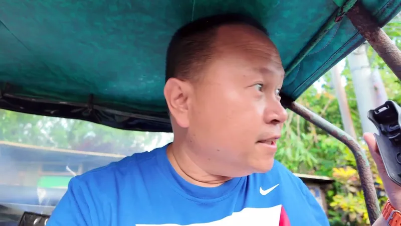 Man in blue shirt riding inside a green tricycle, holding a device, looking right.