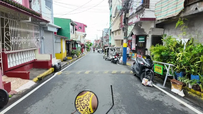 First-person view from a scooter on a wet street lined with colorful buildings and vehicles.