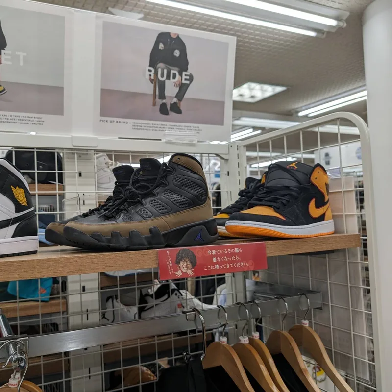 Black and brown, and black and orange high-top sneakers on a shelf at a Japanese second-hand store.