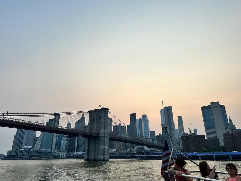 Brooklyn Bridge and lower Manhattan skyline from boat at sunset with American flag