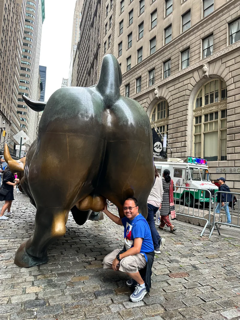 Man smiling while touching Charging Bull statue on Wall Street