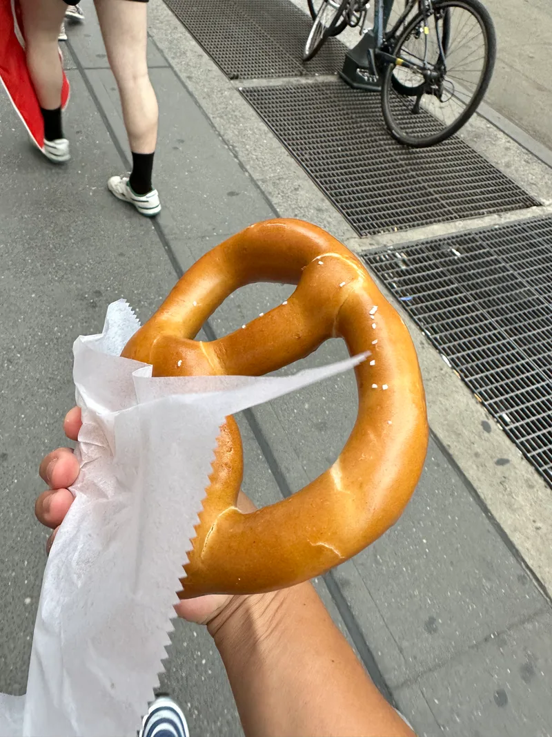 Hand holding a large salted soft pretzel on a New York City street