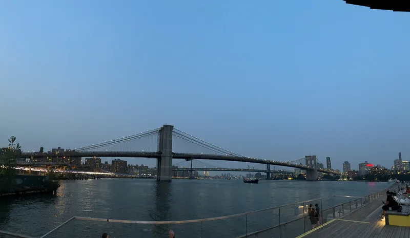 Panoramic view of Brooklyn and Manhattan Bridges with illuminated NYC skyline at dusk