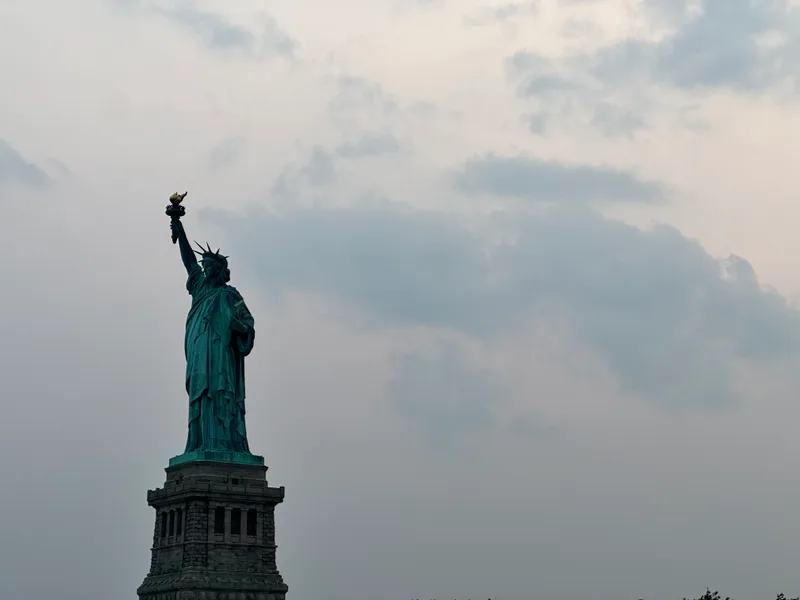 Close-up of Statue of Liberty with green patina and torch against sunset sky