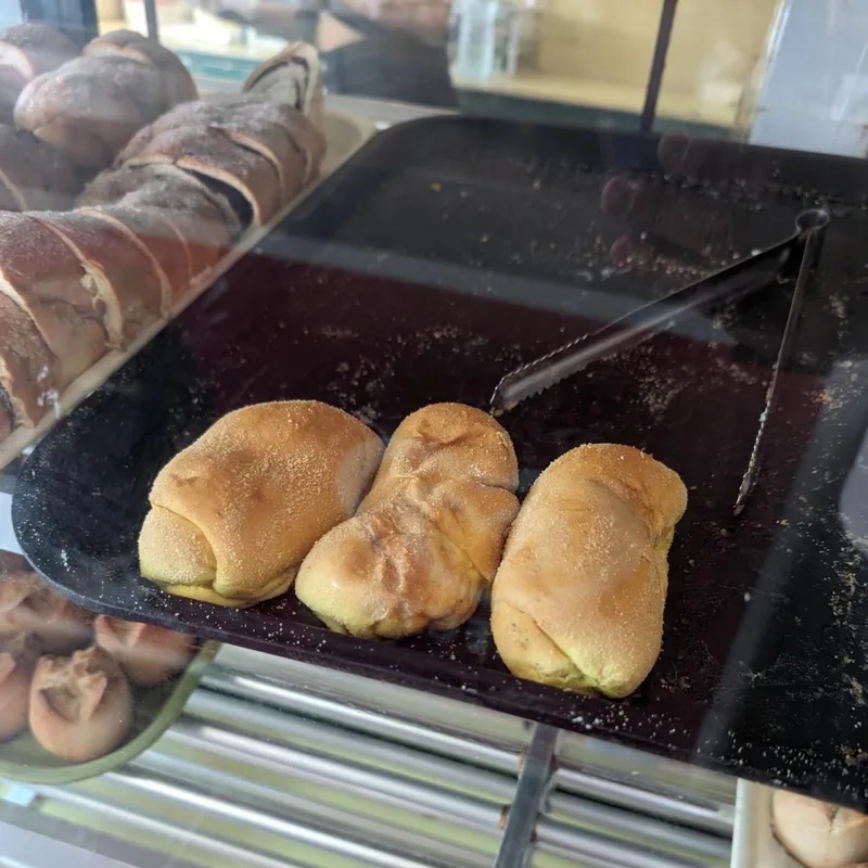 Sugar rolls — simple and exactly right Three golden-brown sugar-dusted bread rolls on a black tray inside a bakery display case in Roxas Palawan Philippines