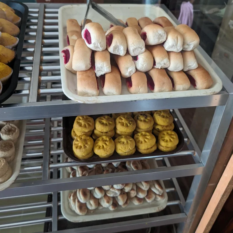 Jam rolls, flower cookies, pan de sal — the full lineup Multi-tiered bakery display case with jam rolls, yellow flower-shaped cookies, and small buns inside Modern Bakery in Roxas Palawan Philippines