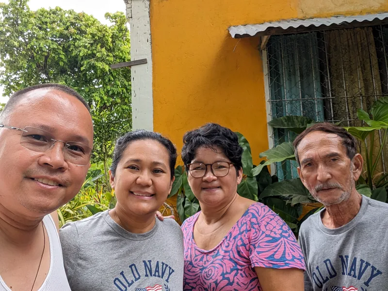 Good people, good day Four people smiling for a group selfie outdoors in front of a bright yellow building with green tropical plants in Roxas Palawan Philippines