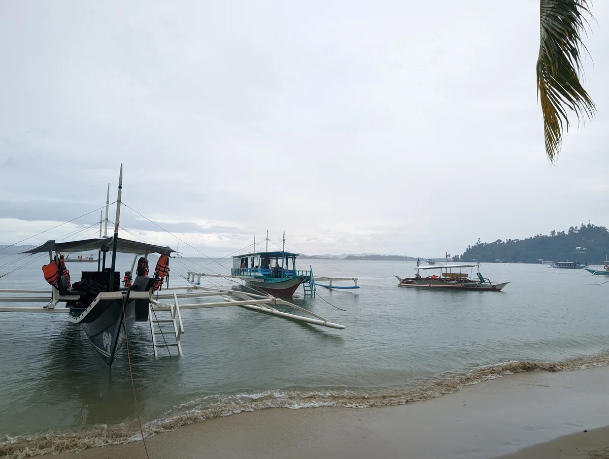 Traditional Filipino outrigger boats anchored in calm grey water at Port Barton beach, Palawan, Philippines
