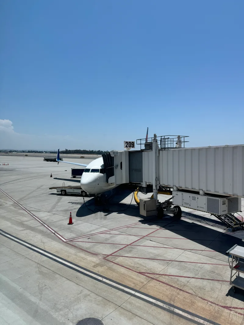 Delta airplane parked at Gate 209 at Ontario International Airport, California, connected to jet bridge under clear blue sky