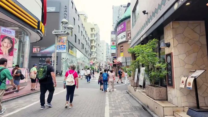Street-level Shibuya, Tokyo, Japan — the side streets are worth exploring People walking along a narrow street in Shibuya, Tokyo, Japan, lined with shops and restaurants, a large tree on the right.