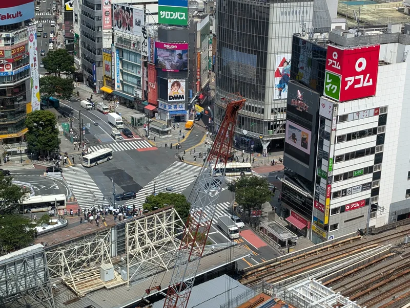 The view straight down at Shibuya intersection from the observation deck — Shibuya, Tokyo, Japan Aerial view of the Shibuya intersection in Tokyo, Japan, from Shibuya Sky, showing pedestrian crosswalks, cars, buses, and surrounding buildings with advertisements.