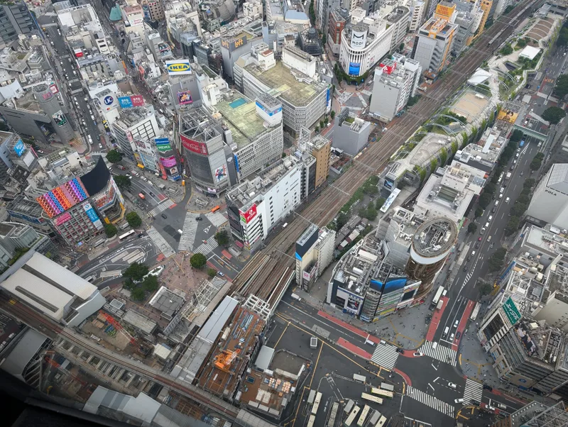 Looking straight down from Shibuya Sky — Tokyo's train network and city grid, Shibuya, Tokyo, Japan High-angle aerial view of dense Tokyo urban area from Shibuya Sky, showing buildings, complex road networks with traffic, and train tracks winding through the city, Shibuya, Tokyo, Japan.