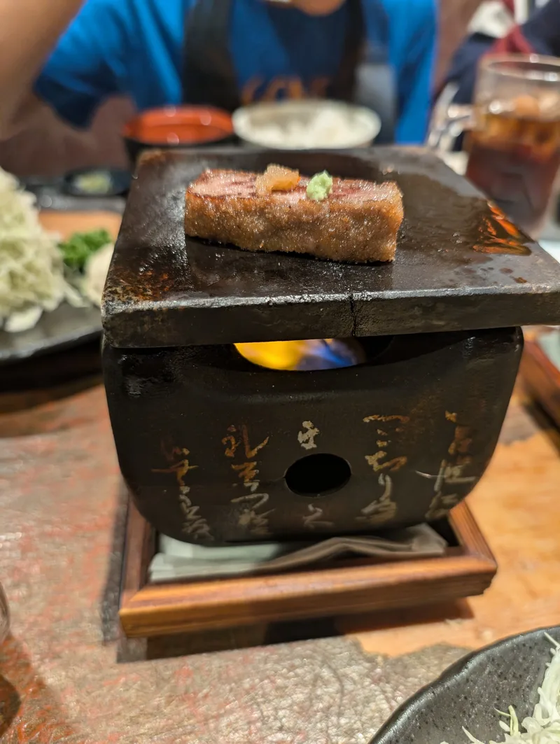 Lunch in Tokyo, Japan Wagyu beef cooking on a personal stone grill with a flame underneath at a Japanese restaurant in Tokyo, Japan, with a small dollop of green condiment on top.