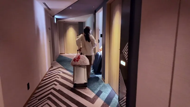 Walking down a modern hotel hallway with geometric carpet pattern pulling suitcases at Hotel Indigo Shibuya, Tokyo, Japan