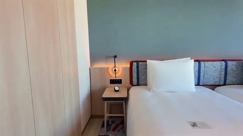 Hotel room with twin beds, wood wardrobe, and blue accent wall showing bedside charging ports at Hotel Indigo Shibuya, Tokyo, Japan