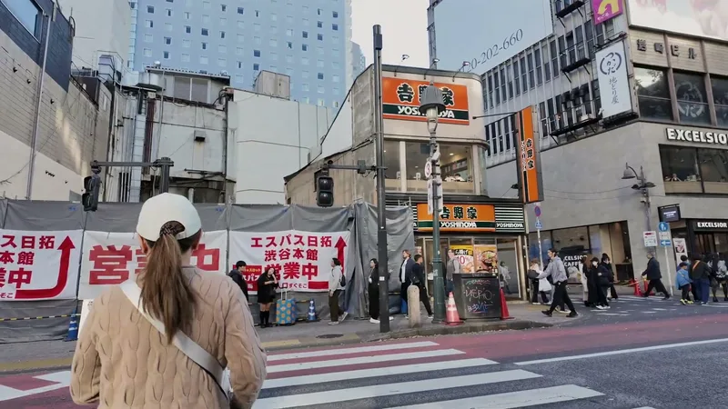 Approaching the Yoshinoya restaurant at a crosswalk in Shibuya with the orange and green sign visible in Tokyo, Japan