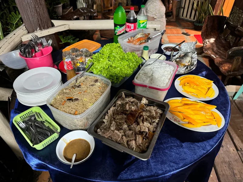 Filipino feast with roasted pig, rice, noodles, mangoes, and drinks on a long table at family gathering in Palawan