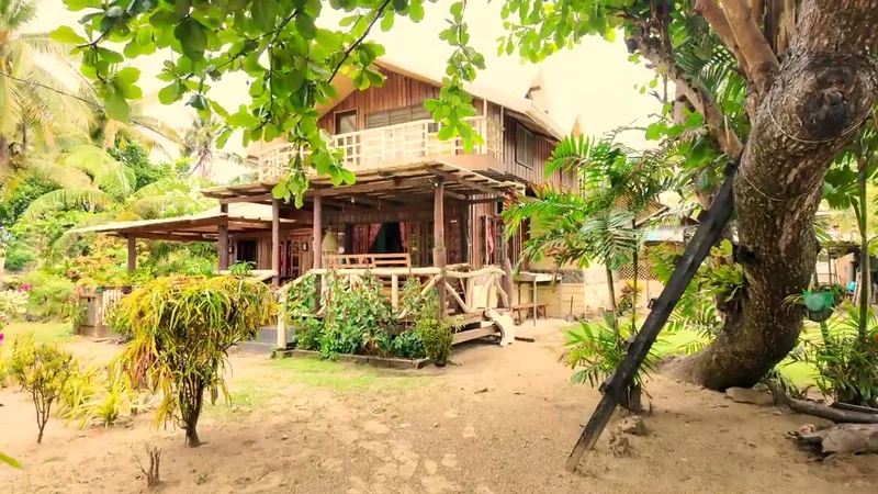 Two-story wooden beach house with porch and balcony surrounded by tropical trees at Uncle Henry's resort in Roxas, Palawan