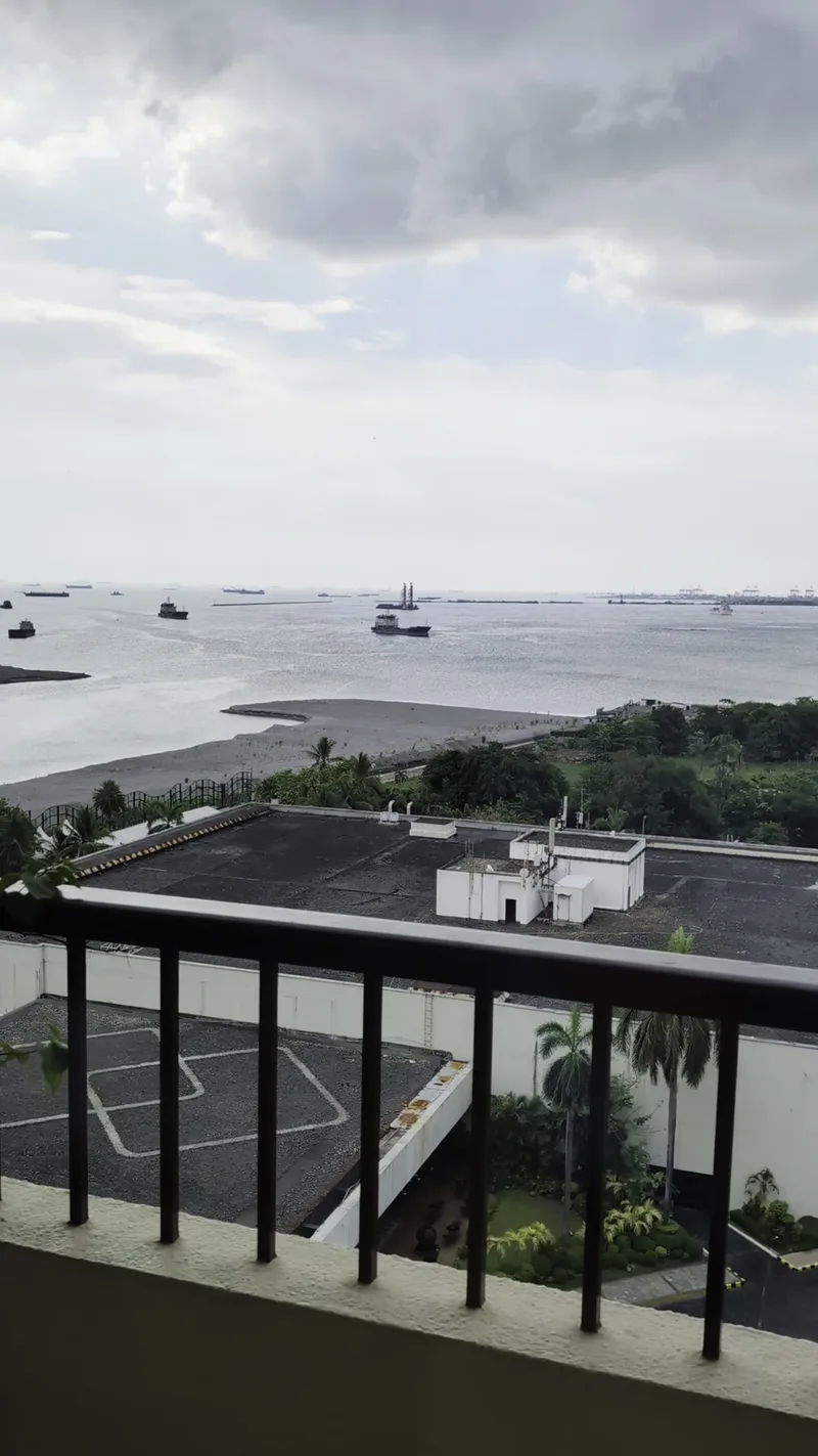 View from the balcony at Sofitel Philippine Plaza overlooking Manila Bay with ships and a sandy shore under a cloudy sky.
